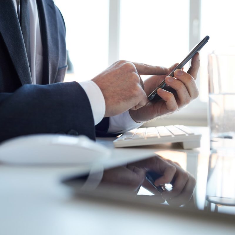 Contemporary office manager or broker with smartphone pointing at touchscreen while using gadget